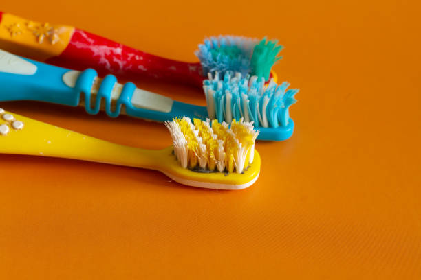 Old used multi-colored toothbrushes with curved bristles that need to be thrown away lie on an orange background stock photo