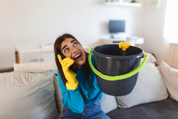 istock Shocked Woman Calling Plumber While Collecting Water Leaking From Ceiling Using Utensil 1421234042