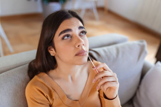 istock woman using cotton swab while doing coronavirus PCR test at home. Woman using coronavirus rapid diagnostic test. Young woman at home using a nasal swab for COVID-19. 1421237354