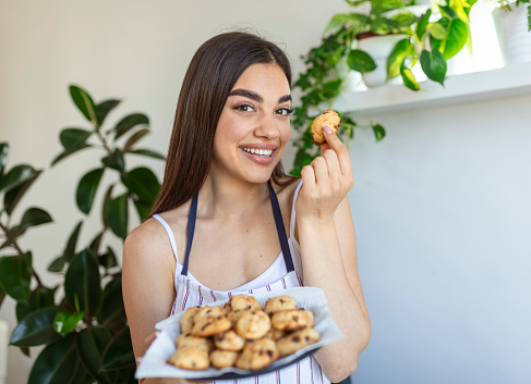 Young beautiful housewife holding freshly baked cookies on a tray in the kitchen.