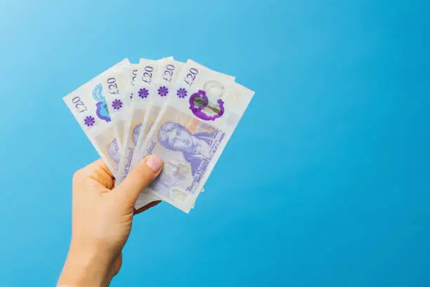 Photo of Image woman's hands which holds British pounds in her hands isolated over blue studio background.