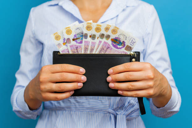 manos femeninas sosteniendo billetes de libras esterlinas en billetera negra sobre un fondo azul. - currency women luxury wealth fotografías e imágenes de stock