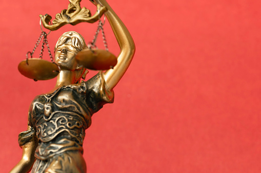 Lady Justice sculpture in front of red background .