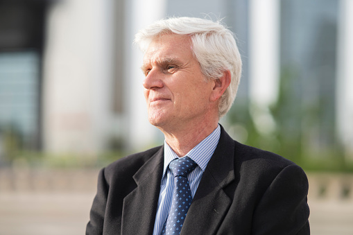 Side view of senior businessman wearing blazer standing against grey background.