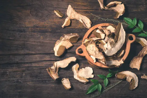 Photo of Dry porcini mushrooms on a rustic antique wooden background, autumn mood. Drying mushrooms for autumn and winter recipes: risotto, soups, stews, pasta. Preservation and preparations for the winter