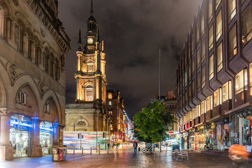Glasgow United Kingdom Ornate historical buildings with clocktower in the pedestrianised part of Buchanan St by night with people visible in blurred motion
