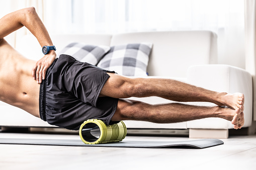 Young man massage lateral thigh muscle with foam roller.