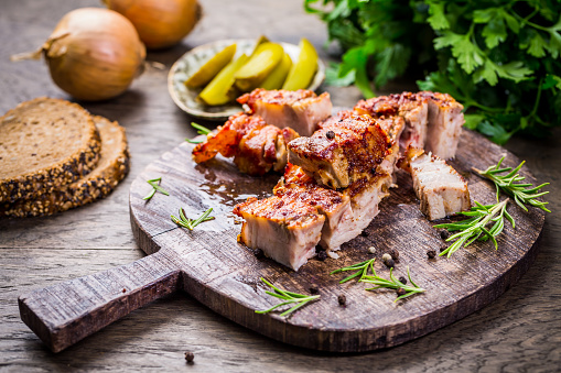 Roasted pork belly with crust and herbs on cutting board