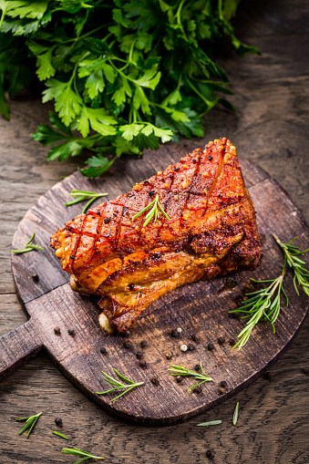 Roasted pork belly with crust and herbs on cutting board