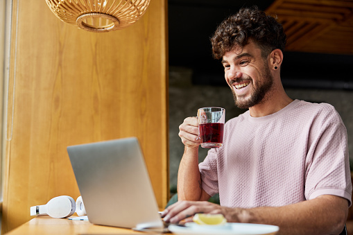 Young happy man drinking tea while reading an e-mail on a computer in a café.