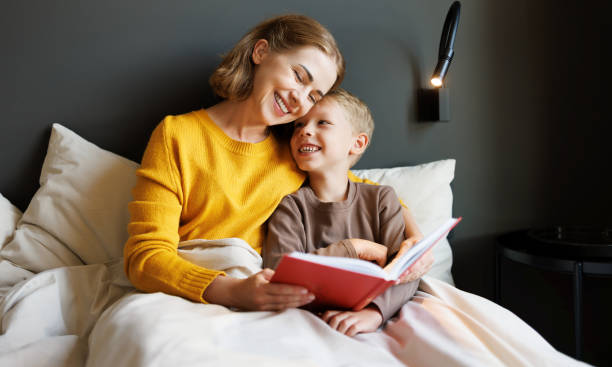 istock Happy mother and son reading book together on bed 1421249217