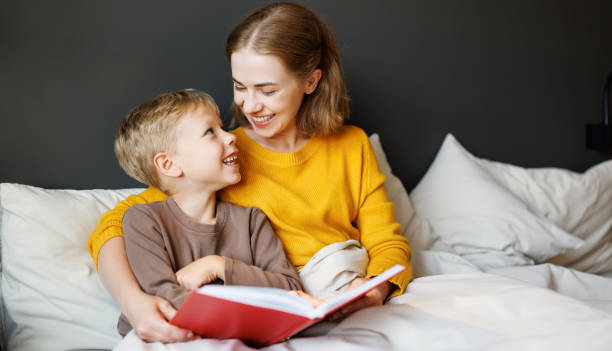 istock Happy mother and son reading book together on bed 1421249348