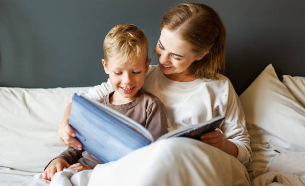 istock Happy mother and son reading book together on bed 1421249478