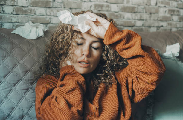 One people at home with flu influenza virus symptoms and neck pain suffering touching body. Health and medicine. Woman sitting on the sofa in cold winter. Young lady with fever disease alone indoor stock photo