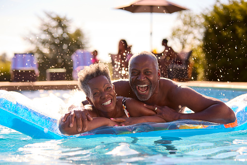 Portrait Of Smiling Senior Couple On Summer Holiday Relaxing In Swimming Pool On Inflatable