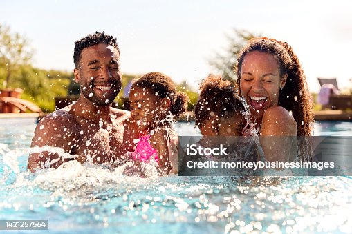 istock Family On Summer Holiday With Two Girls Being Held In Swimming Pool By Parents And Splashing 1421257564