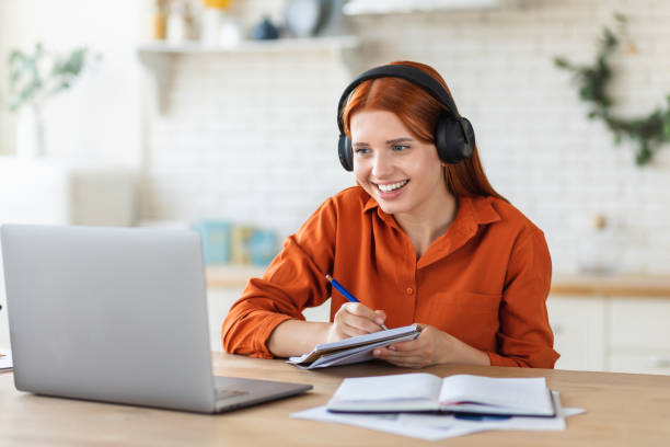 istock Distance learning, online education. Smiling young female student using laptop for studying remotely at home, watching the training, listening to the webinar, video call concept 1421257688