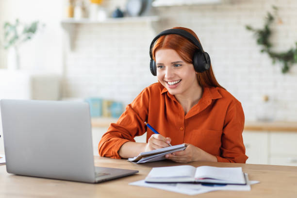 Distance learning, online education. Smiling young female student using laptop for studying remotely at home, watching the training, listening to the webinar, video call concept stock photo