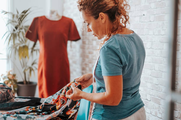 seamstress at home workshop working with clothes in fashion industry. professional tailor making dress. side view of woman in hobby and leisure activity indoor alone. concept of alternative job life - textile textile industry warehouse store imagens e fotografias de stock