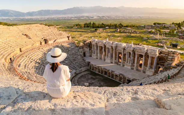 Photo of Hierapolis ancient city Pamukkale Turkey, young woman with hat watching sunset by the ruins Unesco