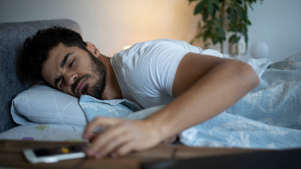 giovane che si sveglia e spegne la sveglia al telefono - dormire troppo foto e immagini stock