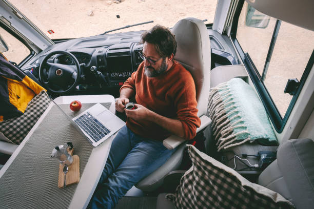 Digital nomad and travel wanderlust lifestyle people concept. One man viewed from above working on laptop and drinking coffee inside a modern camper van. Job and vacation lifestyle. Holiday and work stock photo