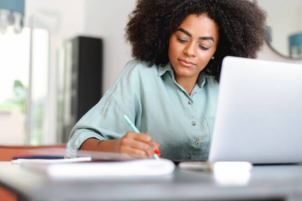 istock Female student watching a lecture, webinar using a laptop, sits at the table and writes with a pen in a notepad 1421266648