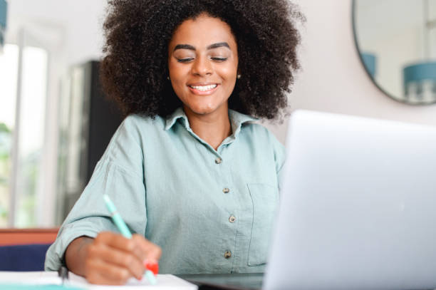 istock Smiling african American female student sits at desk watch webinar taking notes 1421266656