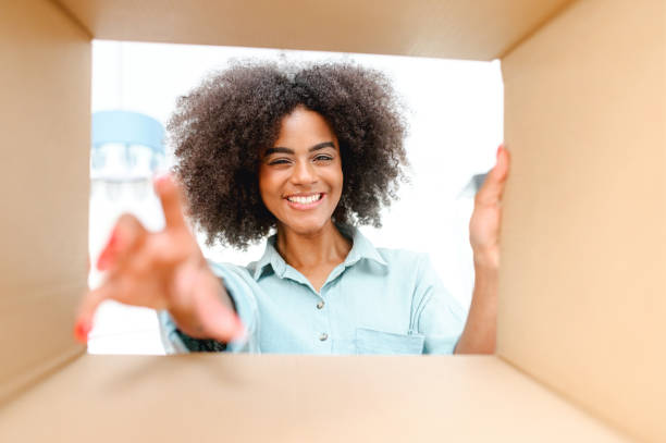 istock Camera inside delivery box, happy African woman taking out parcel from cardboard box 1421266688