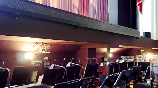 Arrangement of an orchestra pit in the opera and ballet theatre. Empty seats in the orchestra pit during a break in the rehearsal of the musicians. Music stands and notes under the theater stage.