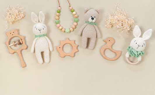 Infant wooden toys and accessories banner on pastel beige background with copy space. Knitted handmade bunny and teddy bear, beads, teethers in eco style on a brown background with raffia clouds.