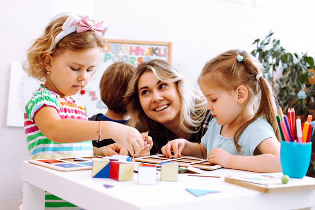 portrait d’une jeune femme heureuse assise à table avec des crayons de couleur jeux de société. professeur regardant une petite fille sérieuse. - number magnet photos photos et images de collection