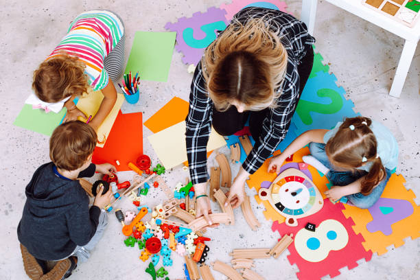 vue de dessus d’une jeune enseignante assise sur le sol avec les enfants des élèves, montrant comment rejoindre un chemin de fer en bois dans la salle de classe. - early childhood education photos et images de collection