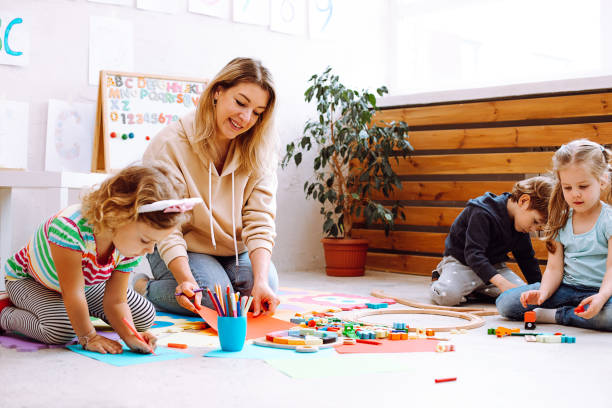 ritratto di giovane insegnante sorridente seduta con bambini meravigliosi, che controlla guardando la pittura su carta rossa. - morning foto e immagini stock