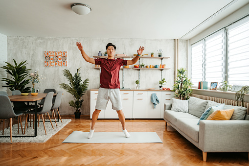 A handsome young Chinese man working out at home. Doing jumping jacks exercise at home.