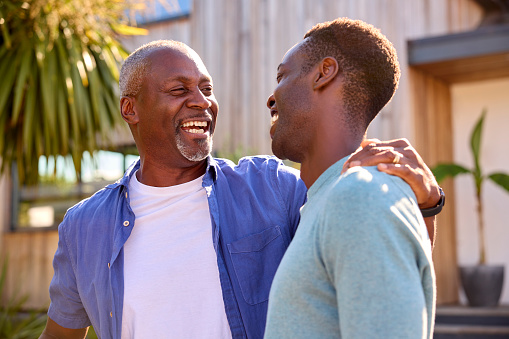 Loving Senior Father With Adult Son Standing Outside House Laughing Together