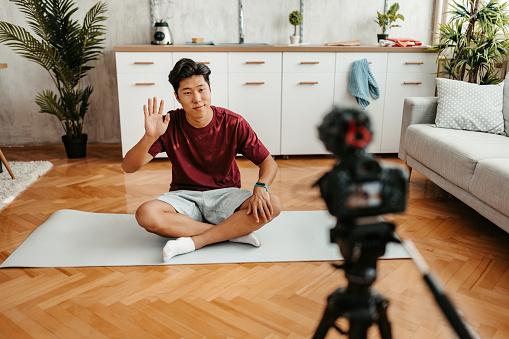 Handsome young Chinese man filming a vlog on working out at home.