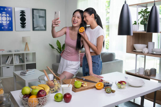 istock Young Asian lesbian couple looking happy while cooking and taking selfie. 1421274500