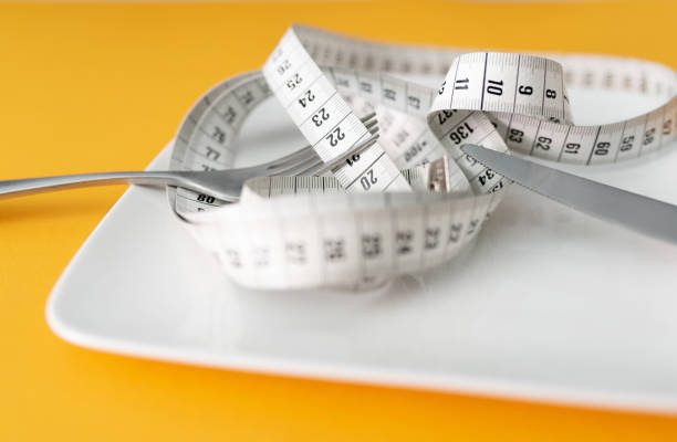 istock tape measure on plate with fork and knife against orange table background 1421278872