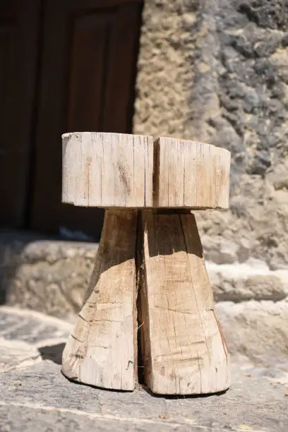 Close-up of a handmade wooden stool. Rural house made of stone is in the background.