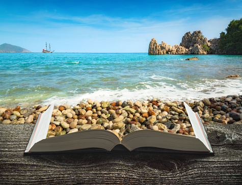 Mediterranean sea coast with ship on the pages of an open magical book. Travel and adventure concept.