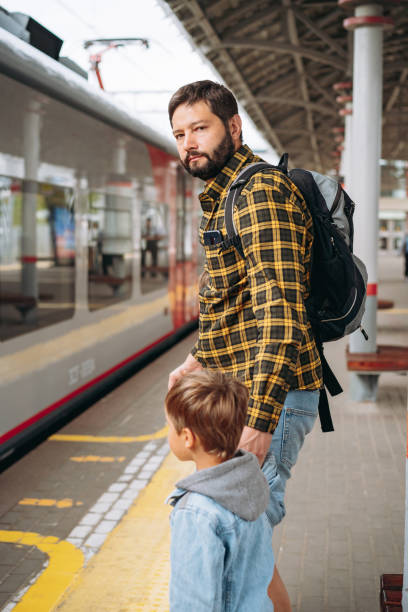 istock caucasian man with backpack holding little son by hand standing at platform going to take train. 1421282853