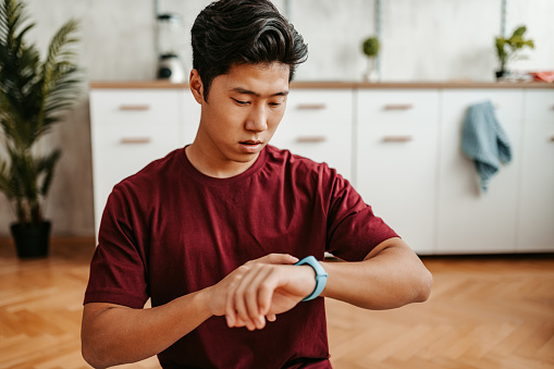 Handsome young Chinese man checking fitness activity on the smart watch after working out at home.