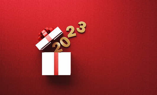 Gold colored 2023 is coming out of a white gift box tied with red ribbon on red background. Horizontal composition with copy space. Directly above. Great use for Christmas related gift concepts.