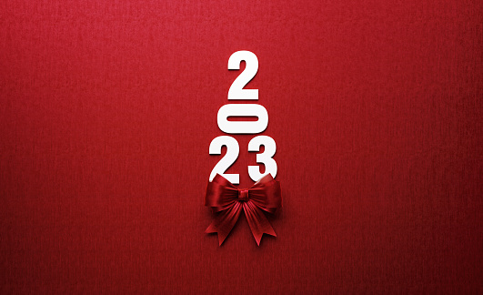 2023 text forming a Christmas tree and is tied with red ribbon on red background. Horizontal composition with copy space. Directly above. Great use for Christmas and 2023 concepts.