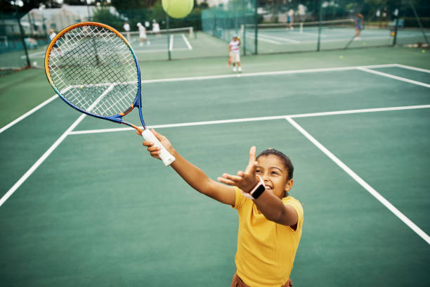 feliz atleta que entrena tenis en una cancha con una pelota y una raqueta durante la práctica de habilidades y técnicas deportivas. juego de fitness, deportes y ejercicios con jóvenes jugadoras disfrutando de un divertido partido al aire libre - tennis child childhood sport fotografías e imágenes de stock