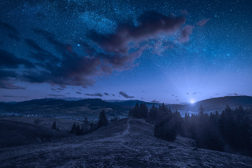 Rising of the full moon in a mountain valley with stars in a cloudy night sky. Dramatic and picturesque scene. Carpathians, Ukraine. Beautiful world.