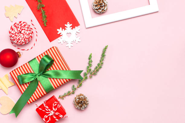 istock Christmas composition. White photo frame, red envelope, fir branches, cones, ball, twine, gift, wooden toys on pink background Flat lay top view. Christmas winter decoration, New Year, holiday objects 1421288534