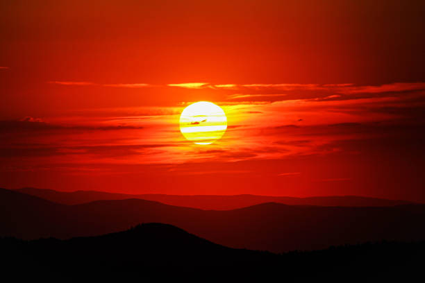 The sun sets over the mountains, in an orange cloud