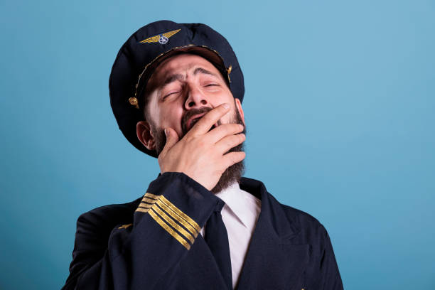 Tired airplane aviator yawning closeup, exhausted pilot covering open mouth with hand. Sleepy aviation academy aircraft captain in aviation uniform with closed eyes front close view